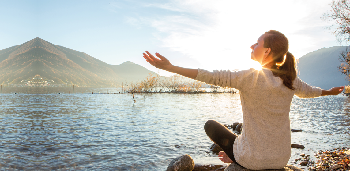 Junge Frau meditiert entspannt an einem See und genießt eine wunderschöne Berglandschaft.