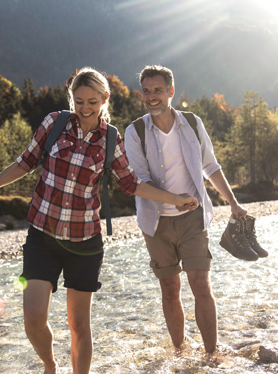 An einem langen Wandertag genießt ein glückliches Paar einen erfrischenden Spaziergang durch einen Fluss.